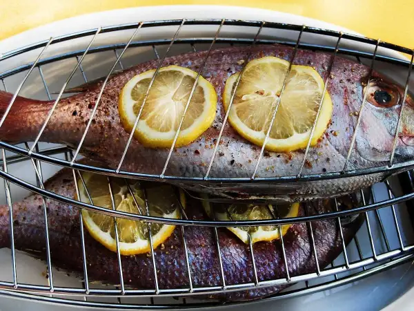 Två hela fiskar ligger på ett grillgaller, toppade med citronskivor. Snart är det dags att grilla fisk!
