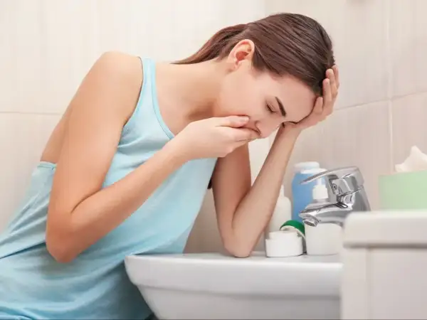 Kobieta w łazience, z ręką na ustach, doświadcza mdłości w ciąży.