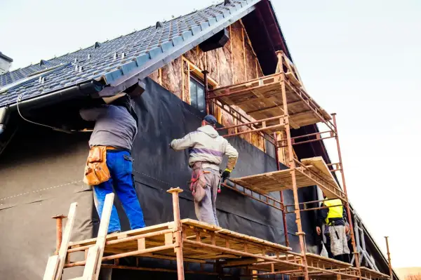 Trois ouvriers sur des échafaudages installent une membrane noire pour l'isolation extérieur, une aide précieuse pour l'efficacité énergétique.