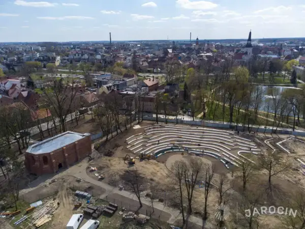 Nowe amfiteatralne trybuny w jarocińskim parku nabierają kształtów. W tle widać panoramę miasta i staw.