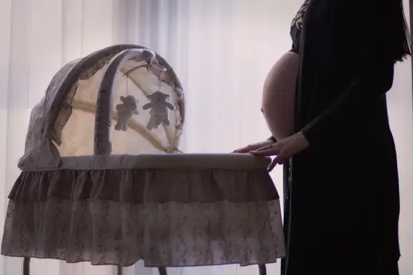 Gravid kvinna med ruckbart huvud vid en vagga med nallar.