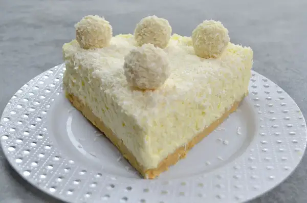 Pyszny sernik Rafaello, udekorowany wiórkami kokosowymi i kulkami przypominającymi Rafaello.