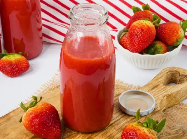 Frische Erdbeeren werden zu einem leckeren Smoothie verarbeitet. Eine Flasche mit dem roten Fruchtgetränk steht bereit.