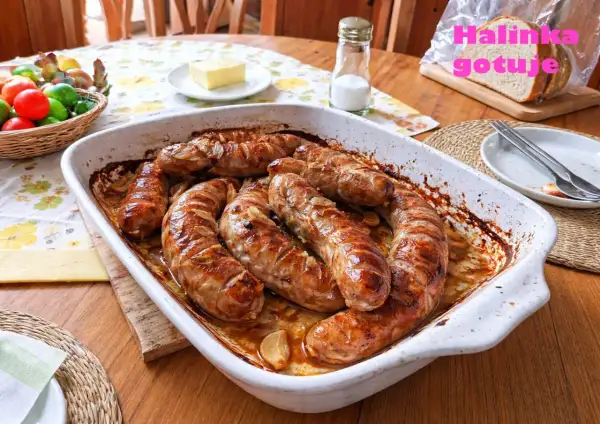 Pyszna, pieczona kiełbasa biała w naczyniu żaroodpornym, z cebulką i czosnkiem. Obok koszyk z jajkami i kromka chleba.