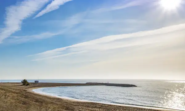 Playa de Macenas en Almería, con un muelle y el sol brillando en el mar.