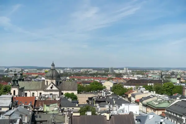 Widok na krakowskie dachy i kościół z kopułą. W tle nowoczesne budynki, które mogą wpływać na ceny mieszkań w Krakowie za m2.