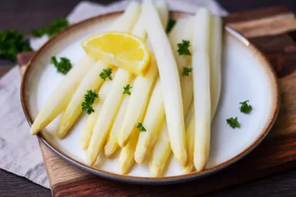 Frischer weißer Spargel, perfekt gegart, mit Zitrone und Petersilie garniert. Ein Genuss, wenn Spargel kochen auf dem Tisch steht.