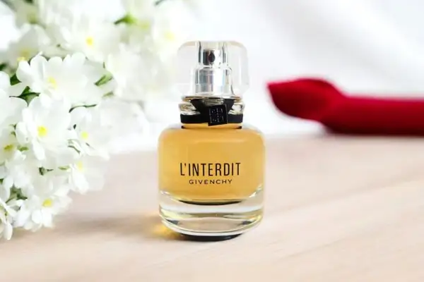 Elegancka butelka Givenchy L'Interdit EDP z białymi kwiatami w tle.
