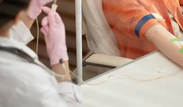 Pierwsza chemioterapia: pielęgniarka w różowych rękawiczkach przygotowuje kroplówkę dla pacjenta.