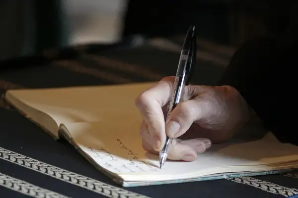 Mano che scrive su un quaderno, un momento intimo che ricorda l'apertura di un testamento olografo.