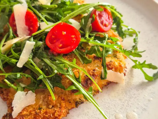Knuspriges paniertes Hähnchen mit Rucola, Kirschtomaten und Parmesan.