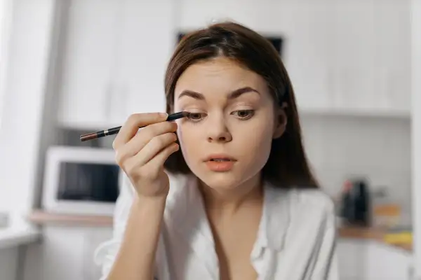 Dziewczyna wykonuje subtelny makijaż typu clean girl, precyzyjnie podkreślając oko kredką.