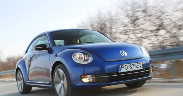 Niebieski, nowy Beetle pędzi po drodze, za nim rozmyty krajobraz drzew.