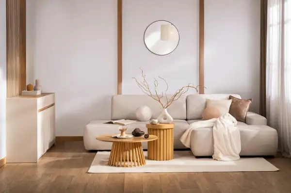 Salon w stylu zen. Jasna kanapa, drewniane stoliki, okrągłe lustro i subtelne dekoracje tworzą oazę spokoju.