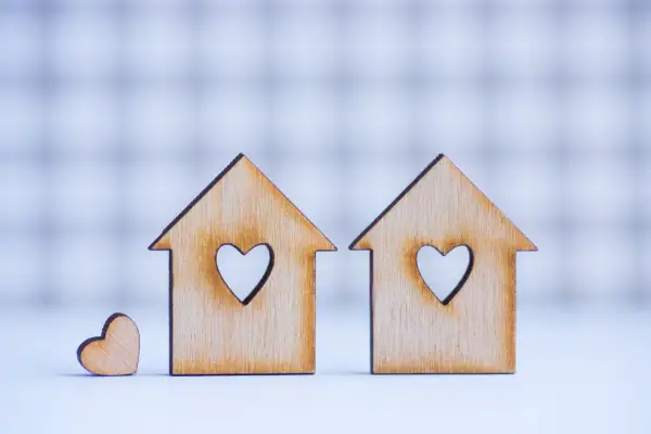 Due casette di legno con cuori intagliati, una più piccola accanto. Simboleggiano la casa e l'amore, ma anche i potenziali conflitti legati ai lavori senza consenso comproprietari.