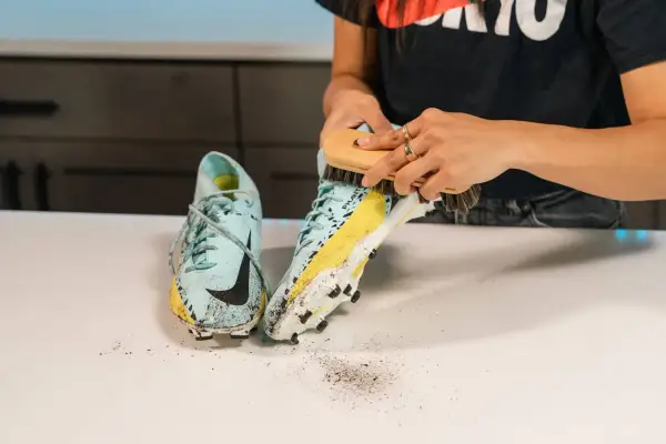 Mani che spazzolano scarpe da calcio sporche di fango, un passo fondamentale per capire come lavare le scarpe da calcio e mantenerle in forma.