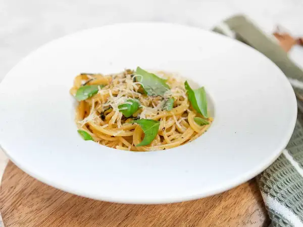 En portion spaghetti alla nerano, krämig och toppad med färsk basilika och riven ost.