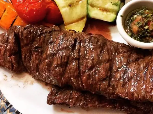 Jugosa entraña de vaca a la parrilla, acompañada de verduras asadas y una salsa chimichurri.