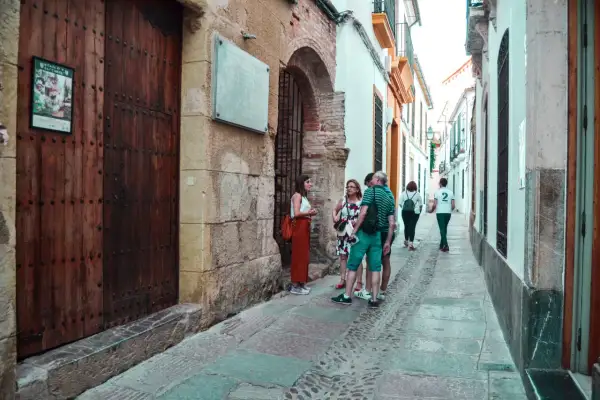 Un grupo de turistas pasea por una calle estrecha y empedrada del quartier juif de Cordoue, admirando la arquitectura antigua.