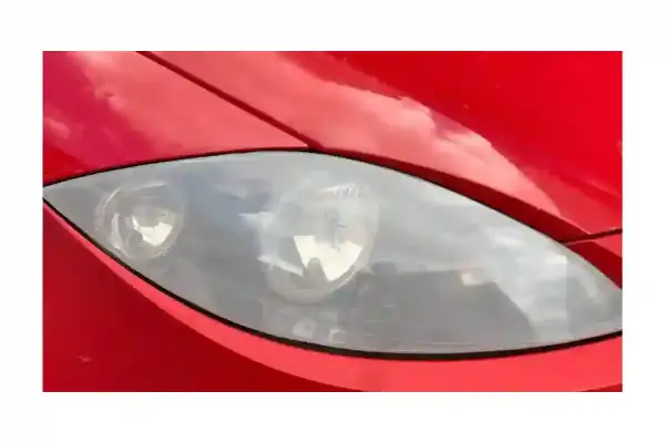 Gros plan sur un phare opaque de voiture rouge, reflétant le ciel.