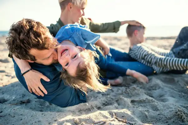 Rodzina na plaży, ojciec tuli córkę, która śmieje się do aparatu. W tle mama i syn. Idealne miejsce na jastrzębia góra atrakcje dla dzieci.