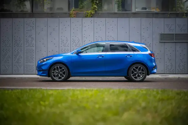 Niebieski hatchback z dynamiczną linią nadwozia, przypominającą coupe, zaparkowany przy nowoczesnej, szarej ścianie.