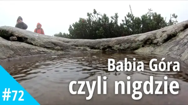Mglisty dzień na Babiej Górze. Dwie osoby w kurtkach przeciwdeszczowych stoją za kamieniem, obok kałuży.