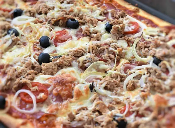 Pyszna pizza z tuńczykiem, oliwkami, cebulą i pomidorami, obficie posypana serem. Idealna na szybki obiad.