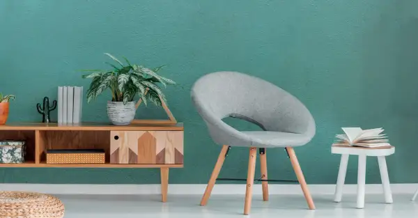 Un angolo relax con sedia grigia, tavolino di legno e un libro aperto, su una parete con pittura satinata color acquamarina.