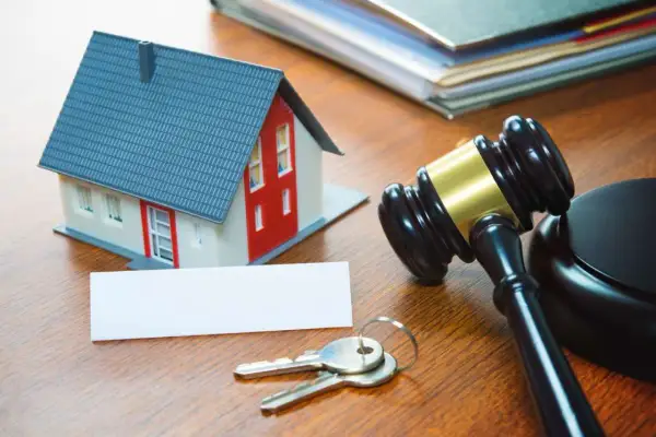 Modellino di casa, chiavi, martelletto da giudice e documenti su un tavolo di legno, evocano aste immobiliari tra privati.