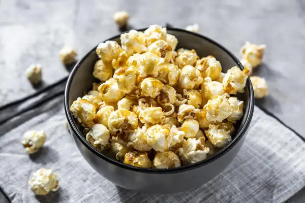 Un bol rempli de pop corn sucré, avec quelques grains éparpillés autour. Parfait pour une soirée cinéma gourmande.