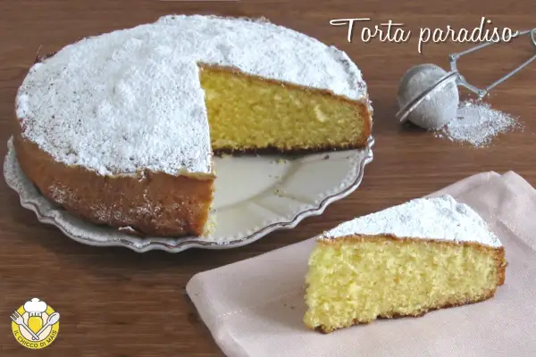 Una soffice torta paradiso, cosparsa di zucchero a velo, attende di essere gustata. Una fetta è già pronta su un tovagliolo rosa.