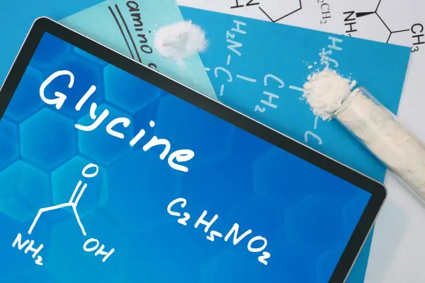 Tablet z napisem "Glycine" i wzorem chemicznym. Obok proszek w probówce. Dowiedz się, glicyna co to za związek.