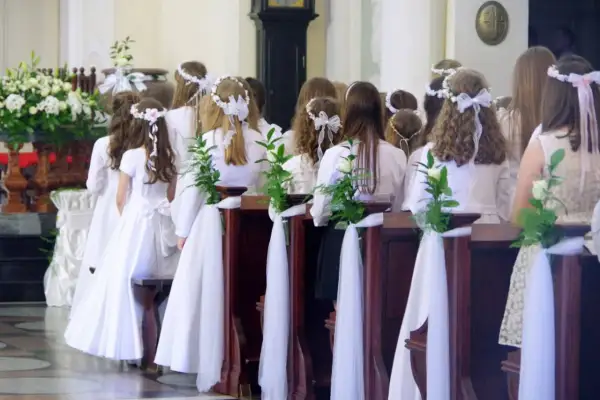 Dzieci w białych strojach, ozdobione wiankami, czekają na komunię. Zazwyczaj do komunii idzie się w wieku około 8-9 lat.