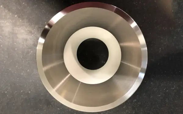 Componente metallico con finitura lucida, probabilmente acciaio inossidabile che contiene nichel, con un inserto bianco al centro.