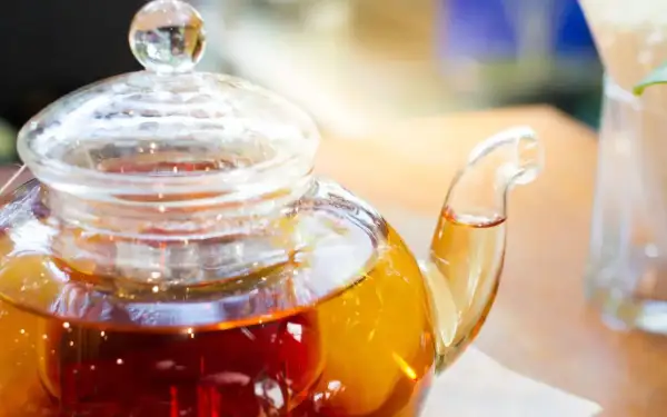 Thé ambré dans une théière en verre, prêt à être servi. La question est : combien d'eau pour un sachet de thé ?