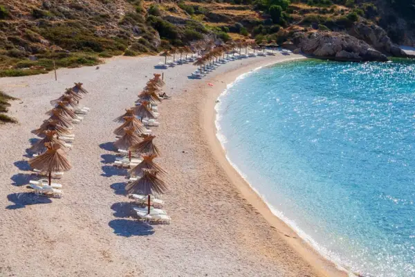 Rząd leżaków pod słomianymi parasolami na kamienistej plaży, obok krystalicznie czystej, turkusowej wody. Jedna z najpiękniejszych plaż w Europie.