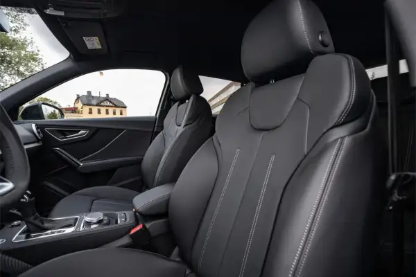 Interni Audi Q2: sedili in pelle nera con cuciture a contrasto, cambio automatico e un edificio storico sullo sfondo.