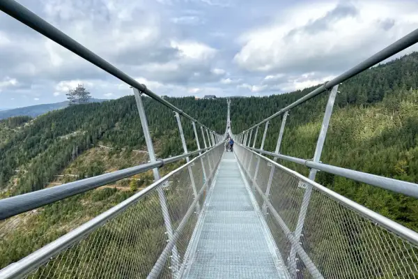 Długa, wisząca konstrukcja Sky Bridge 721 wznosi się nad lasem. Ludzie spacerują po moście, podziwiając widoki.