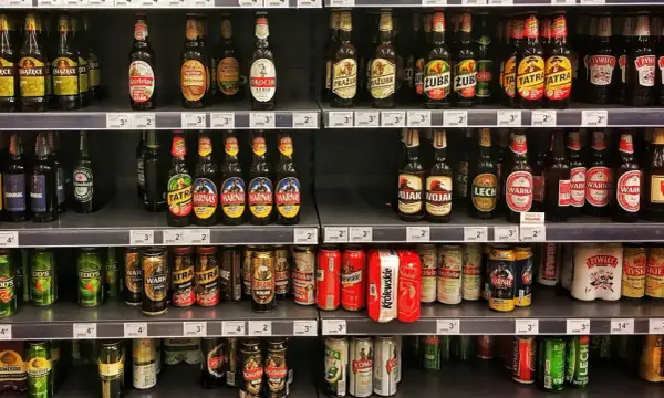 Półki sklepowe uginają się pod ciężarem piwa na półce. Butelki i puszki różnych marek tworzą kolorowy krajobraz.