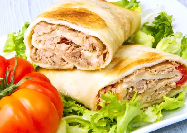 Dos rollos de wrap de atún, rellenos de atún desmenuzado y queso, servidos con lechuga fresca y tomates.