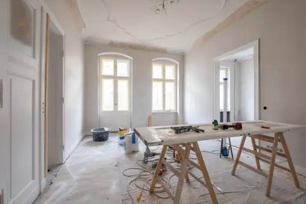 Mieszkanie na sprzedaż do remontu. Wnętrze w trakcie prac, widoczne materiały budowlane, drzwi na kozłach, okna i drzwi z żółtą taśmą.