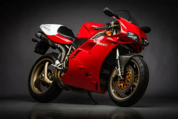 Czerwony motocykl Ducati z białym siedzeniem i złotymi felgami na ciemnym tle.
