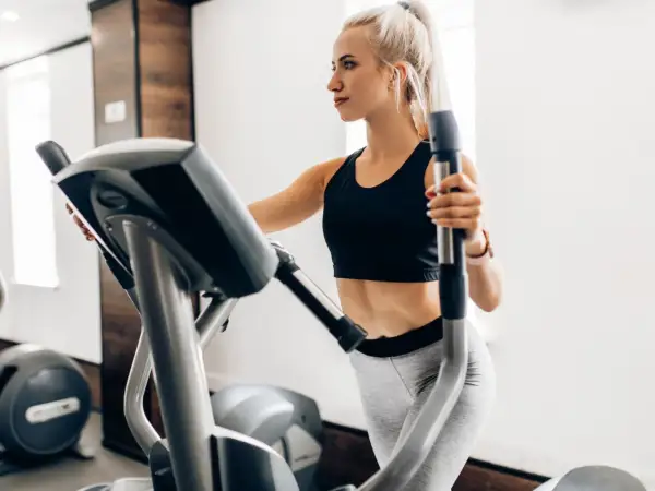 Junge Frau trainiert auf Crosstrainer, um ihren Kalorienverbrauch zu steigern.