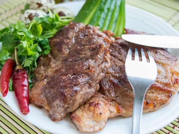 Saftiges Schweinesteak, mariniert und perfekt gegrillt, serviert mit Petersilie, Chilischoten und Wachteleiern. Ein Genuss für Fleischliebhaber.