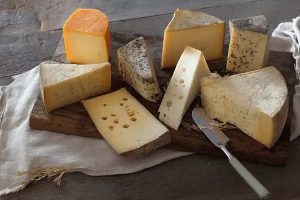 Assortiment de fromages, dont un beau morceau de comté pâte cuite, sur une planche en bois.