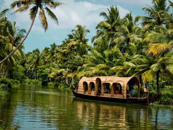 Une péniche navigue sur un canal bordé de palmiers luxuriants. Une belle façon de découvrir que faire au Kerala.