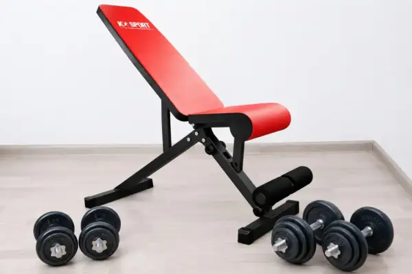 Rote Hantelbank mit schwarzem Rahmen und Hanteln auf dem Boden. Perfekt für dein Home-Gym, die beste Hantelbank für dein Training.