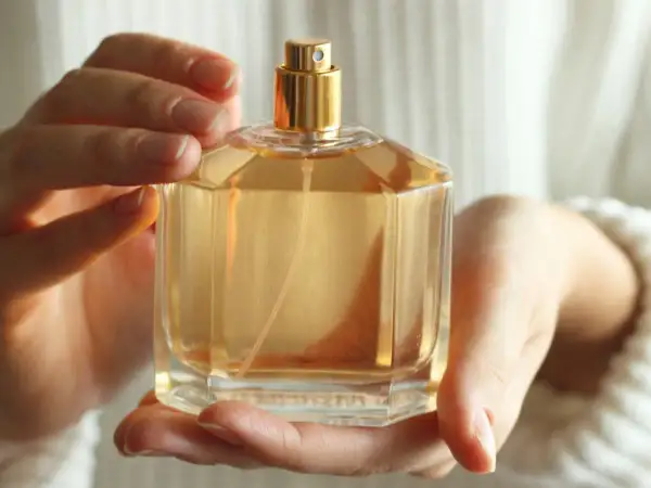 Dłonie trzymają elegancką butelkę z płynem w kolorze bursztynu. To idealny dodatek, który podkreśli Twój styl. Data perfum.