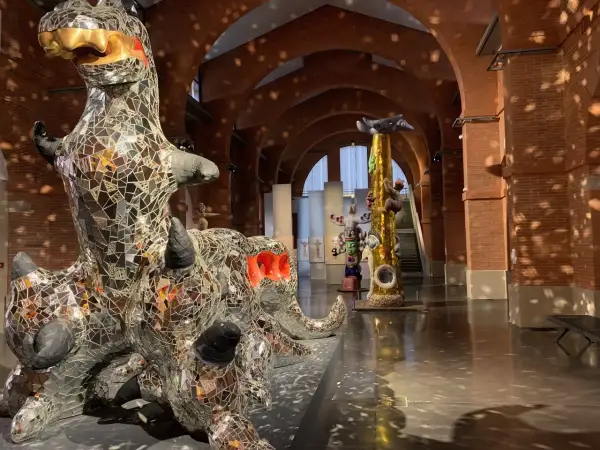 Sculptures de Niki de Saint Phalle, dont un dragon miroitant, dans un musée aux arches de briques.